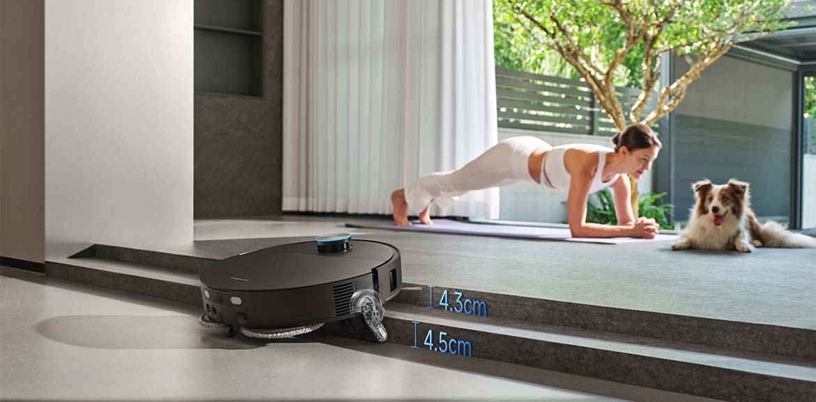 Robot sprzątający pokonuje próg między poziomami podłogi, obok ćwiczącej kobiety i psa